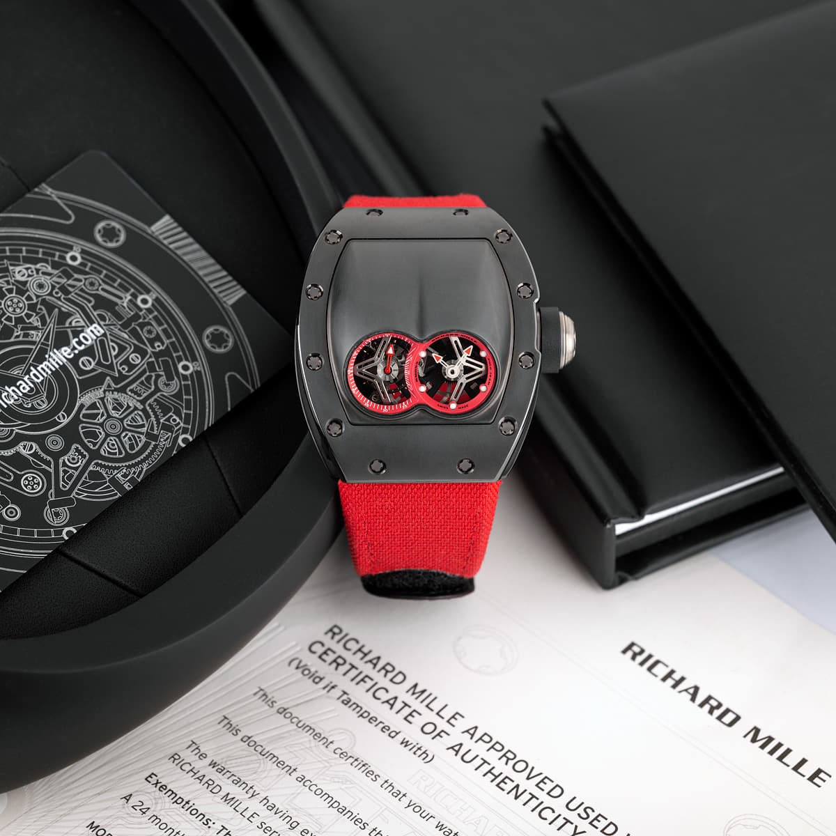 Piece unique Richard Mille RM053 black titanium case with twelve visible black screws, red velcro strap, two raised arcs with red accents. The watch is placed on top of certificate.
